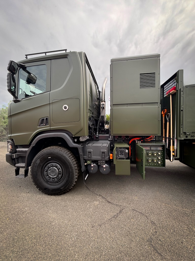 Militärgrön hybridlastbil från Scania med GridLink installerad bakom hytten för mobil energiförsörjning.